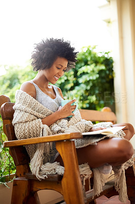 Buy stock photo Shot of a young woman relaxing with a book and a cup of coffee at home