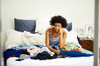 Buy stock photo Shot of an unhappy young woman getting dressed with piles of clothing on her bed