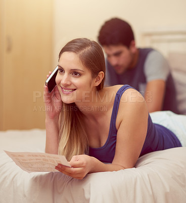Buy stock photo Shot of a happy young woman talking on her cellphone while lying on her bed at home
