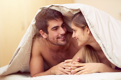 Buy stock photo Shot of a loving young couple smiling at each other while lying under a blanket together