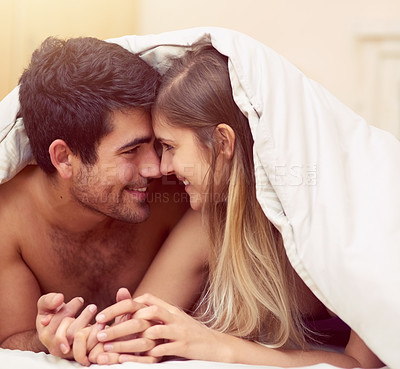 Buy stock photo Shot of a loving young couple smiling at each other while lying under a blanket together