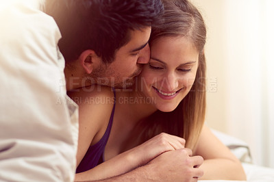 Buy stock photo Shot of a loving young couple sharing a kiss while lying under a blanket together