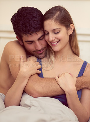 Buy stock photo Shot of a loving young couple sharing an intimate embrace while sitting in bed