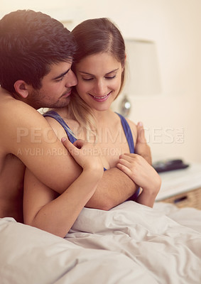 Buy stock photo Shot of a loving young couple sharing an intimate embrace while sitting in bed