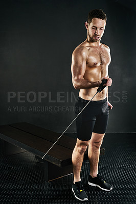 Buy stock photo Studio shot of a shirtless young man working out with a resistance band against a dark background