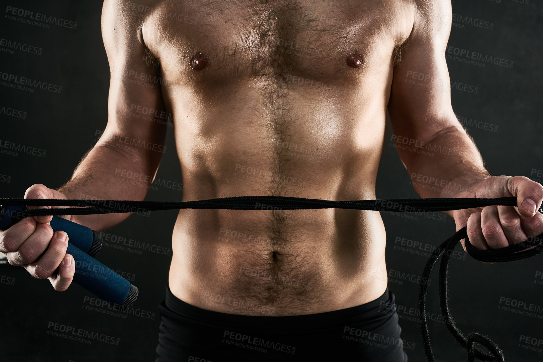 Buy stock photo Studio shot of a man's torso while holding a skilpping rope against a dark background