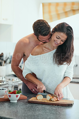 Buy stock photo Shot of a loving young man embracing his girlfriend from behind while she makes breakfast in the kitchen