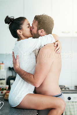 Buy stock photo Shot of a loving young couple sharing an intimate kiss in their kitchen at home