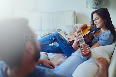 Buy stock photo Shot of a young woman playing guitar for her boyfriend while sitting together on the sofa at home