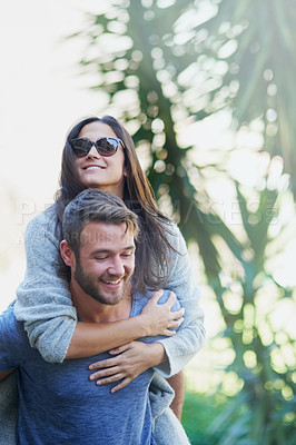 Buy stock photo Shot of a young man giving his girlfriend a piggyback while enjoying a day together outside