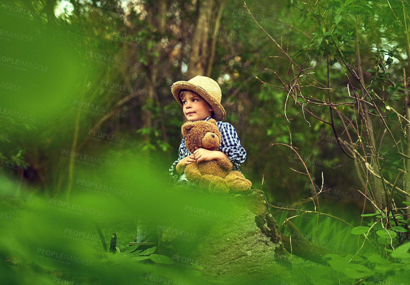 Buy stock photo Calm, young boy and teddy bear in forest with straw hat for outdoor adventure and exploration in nature. Excited, male child or smile for hug with stuffed animal in woods for fun, relax and discovery