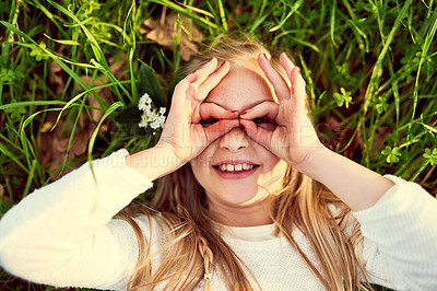 Buy stock photo Finger glasses, portrait and happy girl on grass from above to relax in summer for child development. Face, hand gesture and smile with playful kid lying on lawn outdoor in garden, nature or park