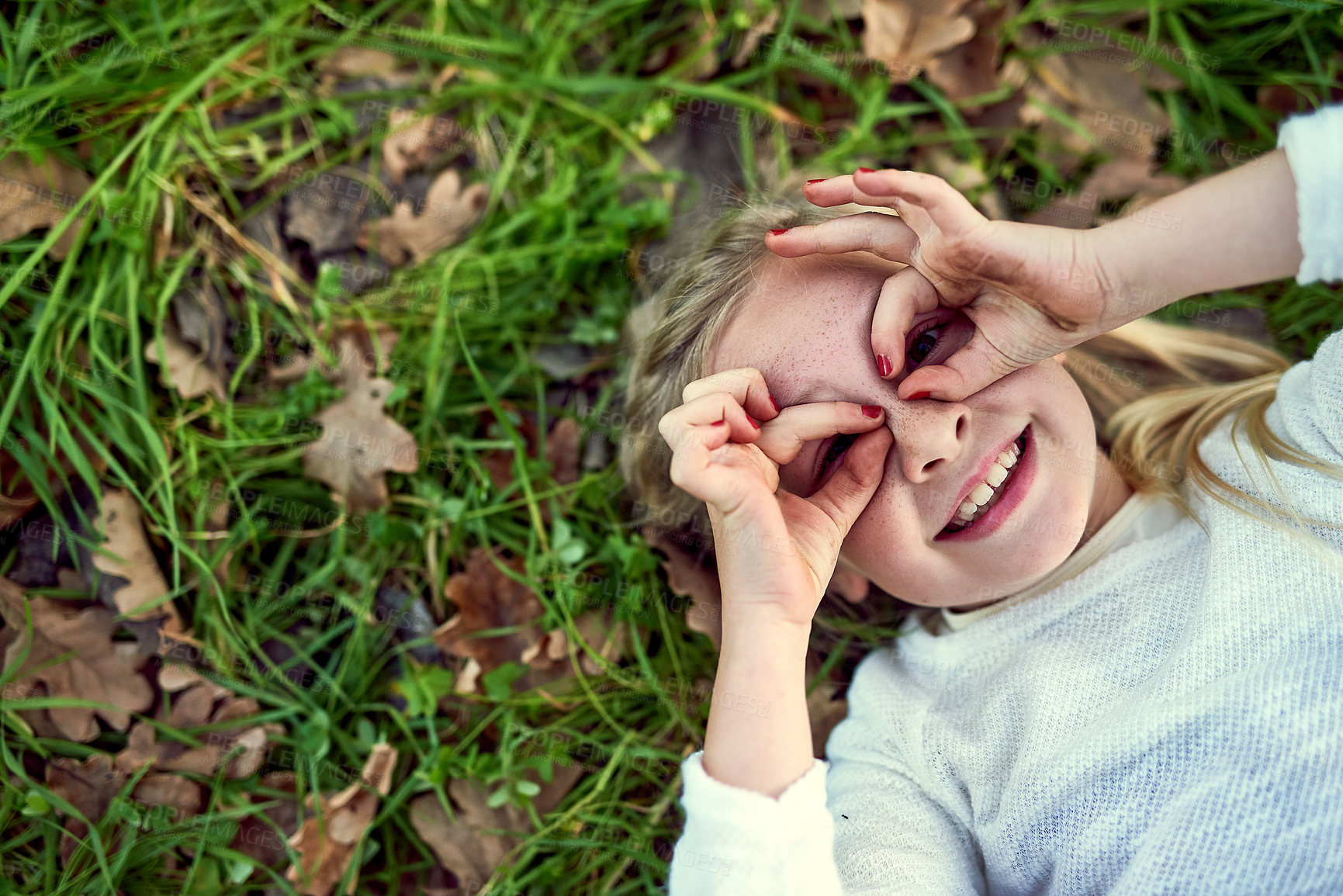 Buy stock photo Finger glasses, portrait and happy girl on lawn from above to relax in summer for child development. Face, hand gesture and smile with playful kid lying on grass outdoor in garden, nature or park