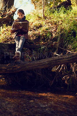 Buy stock photo Shot of a young girl reading a book outdoors