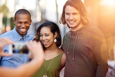 Buy stock photo Shot of a group of young friends having their picture taken on a smart phone
