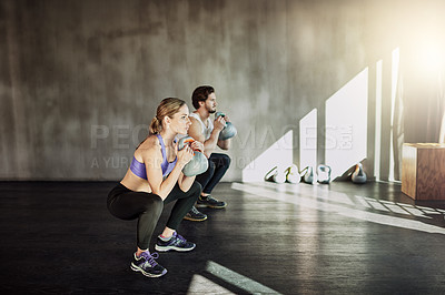 Buy stock photo Shot of two young people working out in the gym using kettle bells