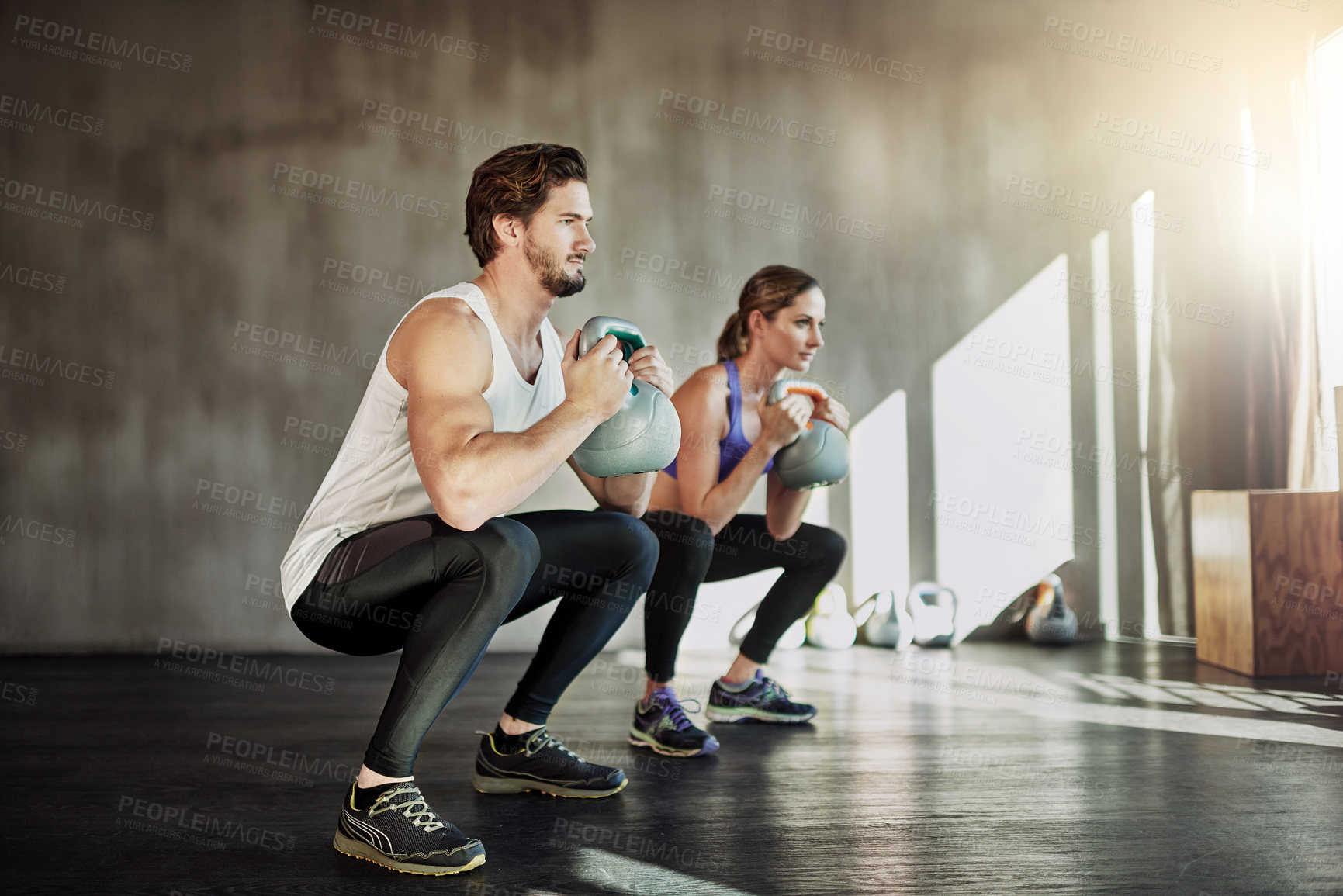 Buy stock photo Shot of two young people working out in the gym using kettle bells