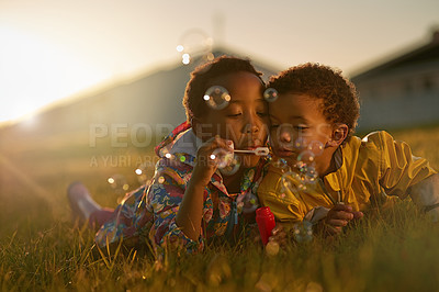 Buy stock photo Shot of a brother and sister lying on the ground outside blowing bubbles