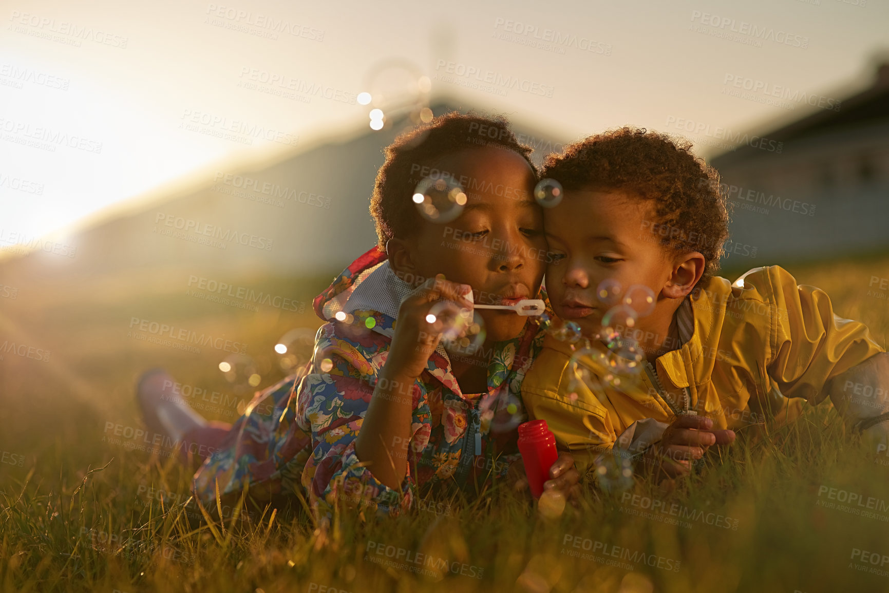 Buy stock photo Shot of a brother and sister lying on the ground outside blowing bubbles