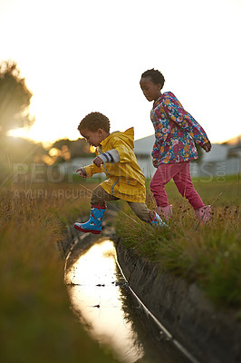 Buy stock photo Shot of a brother and sister jumping over water while playing outside