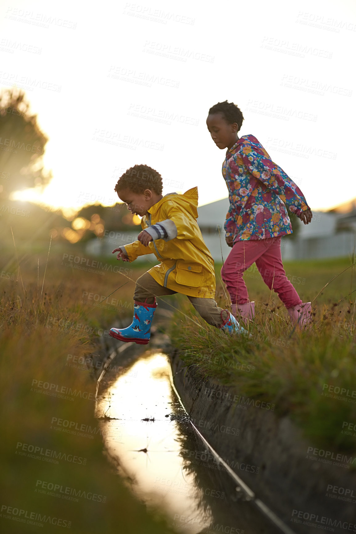 Buy stock photo Shot of a brother and sister jumping over water while playing outside