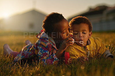 Buy stock photo Nature, sunset and children blowing bubbles in park relaxing on grass together for bonding. Family, fun and kid siblings playing with soap toy laying on lawn in outdoor garden or field in evening.