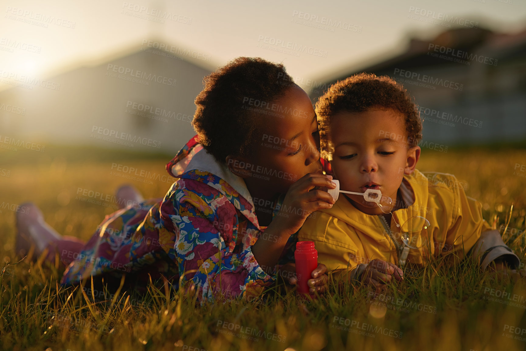 Buy stock photo Nature, sunset and children blowing bubbles in park relaxing on grass together for bonding. Family, fun and kid siblings playing with soap toy laying on lawn in outdoor garden or field in evening.