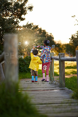 Buy stock photo Shot of a little brother and sister walking away over a bridge blowing bubbles