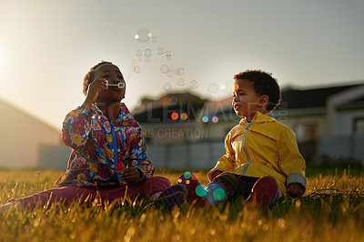 Buy stock photo Nature, sunset and kids blowing bubbles in park relaxing on grass together for bonding. Family, fun and children siblings playing with soap toy laying on lawn in outdoor garden or field in evening.