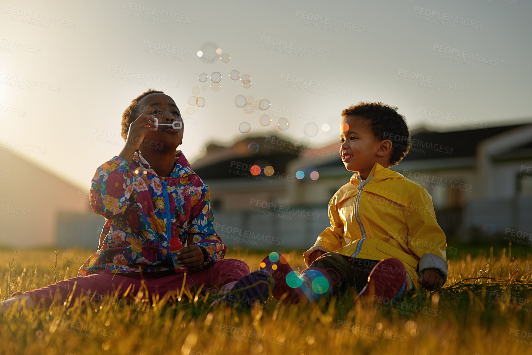 Buy stock photo Nature, sunset and kids blowing bubbles in park relaxing on grass together for bonding. Family, fun and children siblings playing with soap toy laying on lawn in outdoor garden or field in evening.