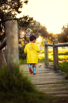 Buy stock photo Shot of a little boy walking away over a bridge blowing bubbles