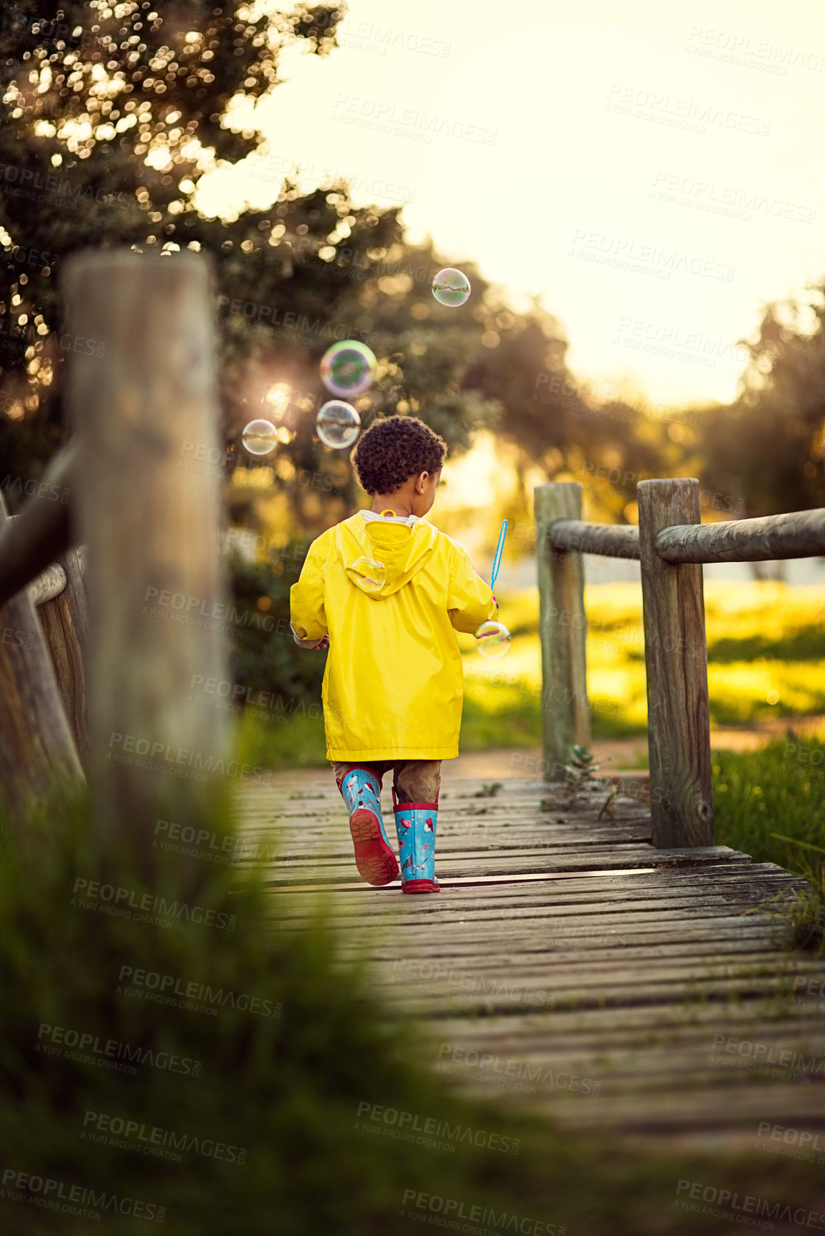 Buy stock photo Shot of a little boy walking away over a bridge blowing bubbles