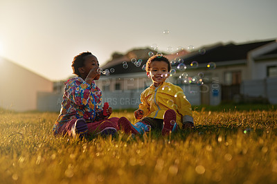 Buy stock photo Shot of a brother and sister sitting on the ground outside blowing bubbles