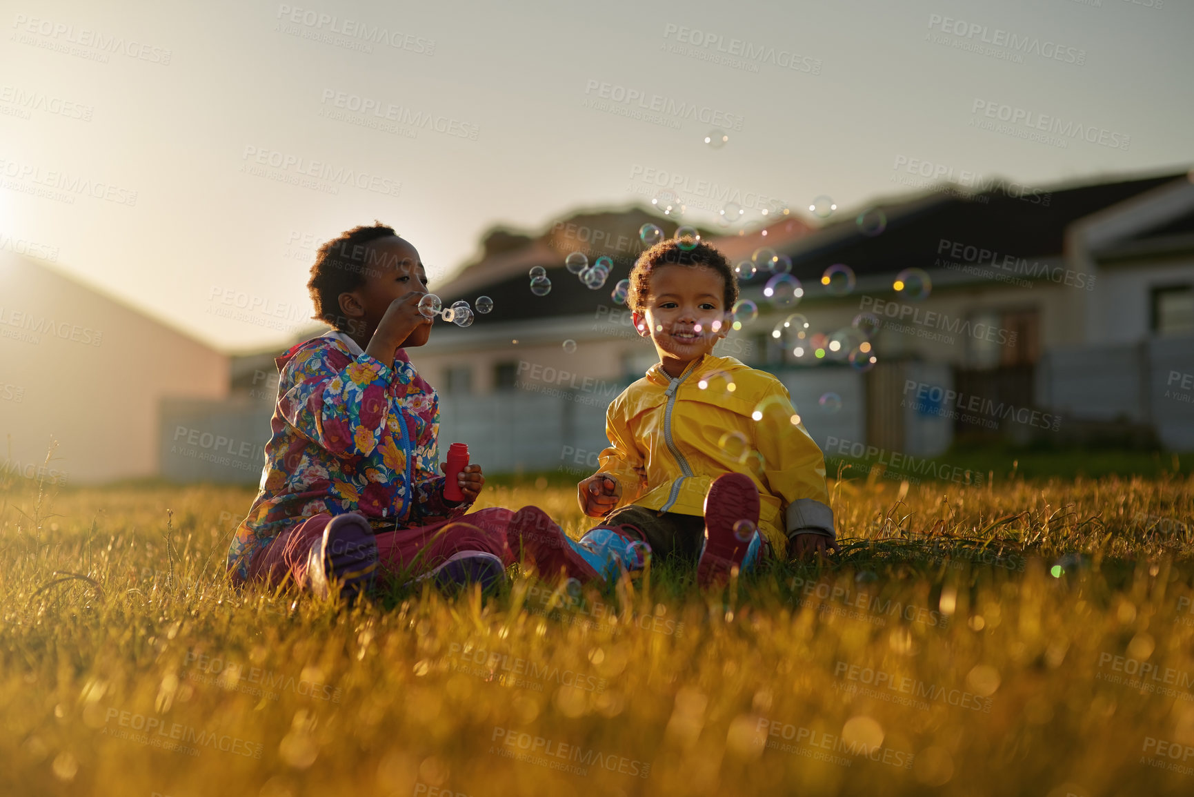 Buy stock photo Shot of a brother and sister sitting on the ground outside blowing bubbles