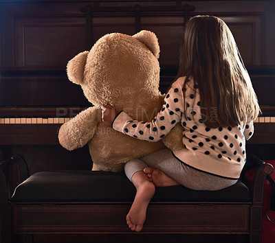 Buy stock photo Rear view shot of a little girl sitting in front of a piano with her teddy bear