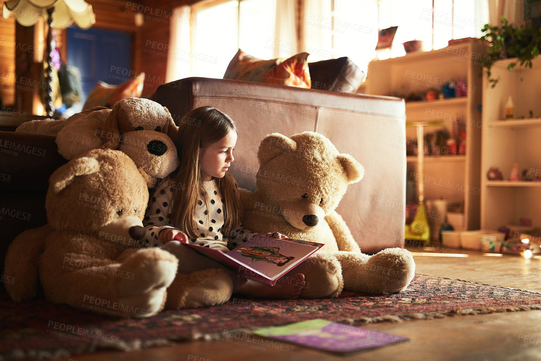 Buy stock photo Shot of a little girl reading a book with her teddy bears around her