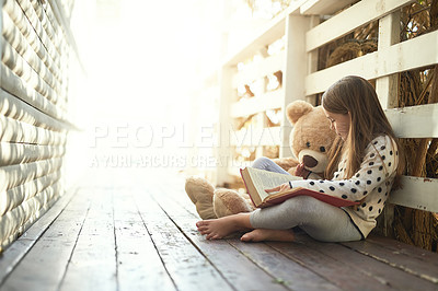 Buy stock photo Shot of a little girl reading a book with her teddy bear beside her