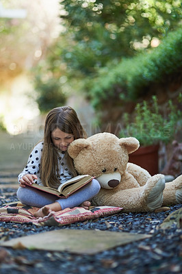 Buy stock photo Shot of a little girl reading a book with her teddy bear beside her