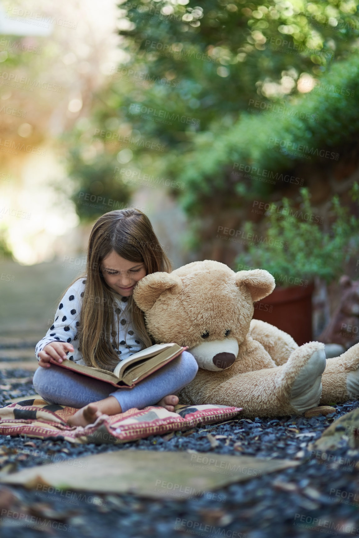 Buy stock photo Shot of a little girl reading a book with her teddy bear beside her