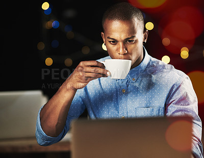 Buy stock photo Shot of a young man drinking an espresso while working late night on his laptop