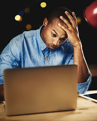 Buy stock photo Shot of a young man looking stressed while working late night on his laptop
