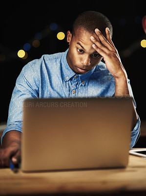 Buy stock photo Shot of a young man looking stressed while working late night on his laptop