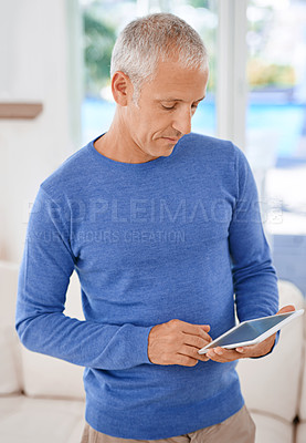 Buy stock photo Shot of a mature man standing in his living room using a digital tablet