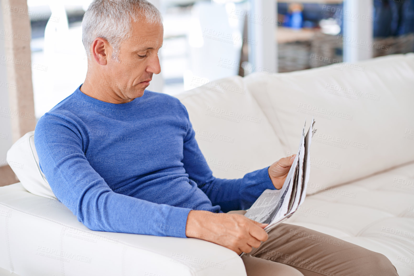 Buy stock photo Shot of a mature man sitting on his living room sofa reading a newspaper