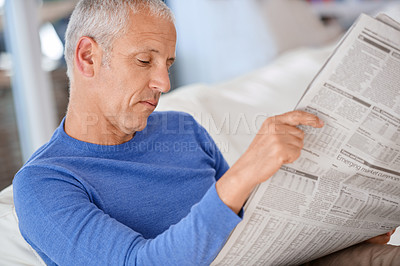 Buy stock photo Senior, man and reading a newspaper on sofa for article, information and morning routine in living room of home. Elderly, person and media paper for global news, knowledge or relax on couch in lounge