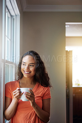 Buy stock photo Shot of a smiling young woman looking through a window while drinking a coffee at home