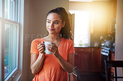 Buy stock photo Shot of a smiling young woman looking through a window while drinking a coffee at home