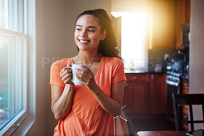 Buy stock photo Shot of a smiling young woman looking through a window while drinking a coffee at home