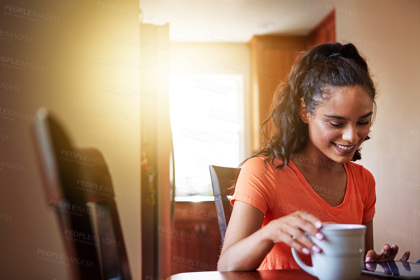 Buy stock photo Shot of a smiling young woman sitting at her dining table at home drinking coffee and using a digital tablet