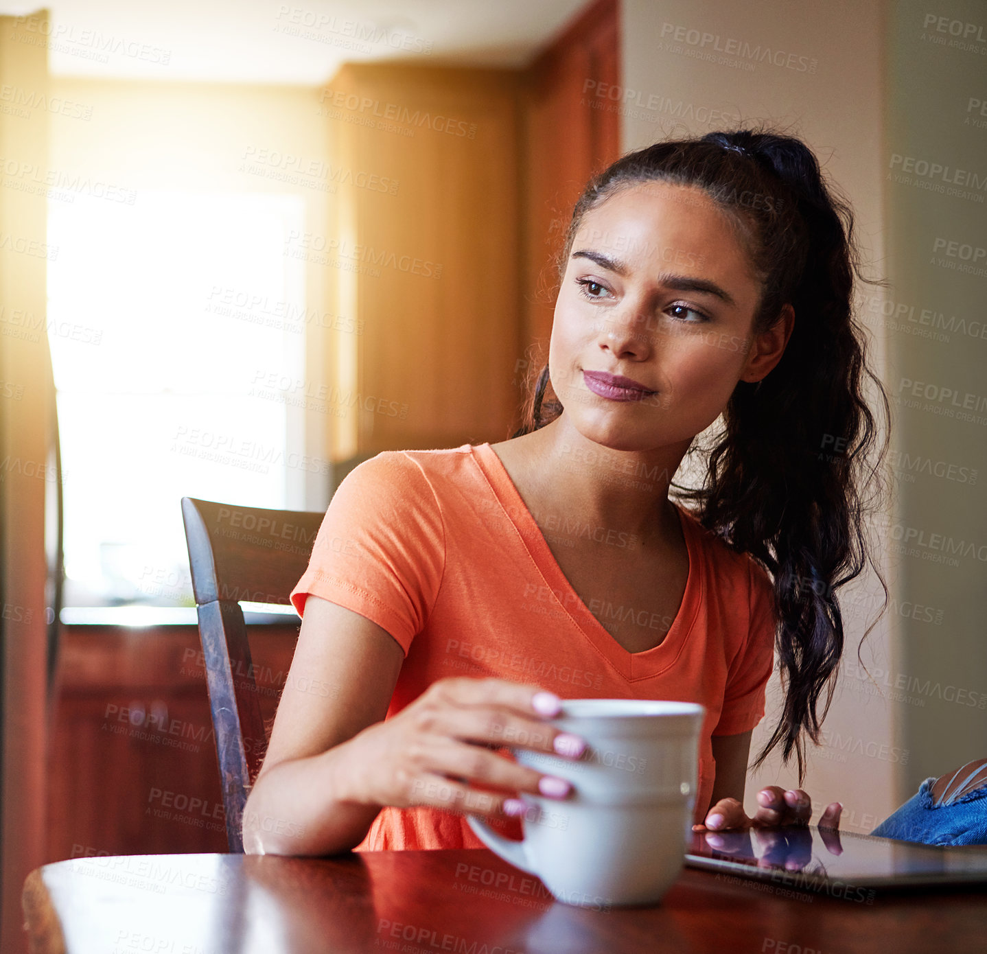 Buy stock photo Shot of a smiling young woman sitting at her dining table at home drinking coffee and using a digital tablet